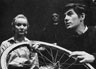 Jennifer Hilary as Zoe watches unseeingly as her stepbrother Godfrey (Ian McKellen) mends a puncture. In the background, the Priest is played by Peter Howell